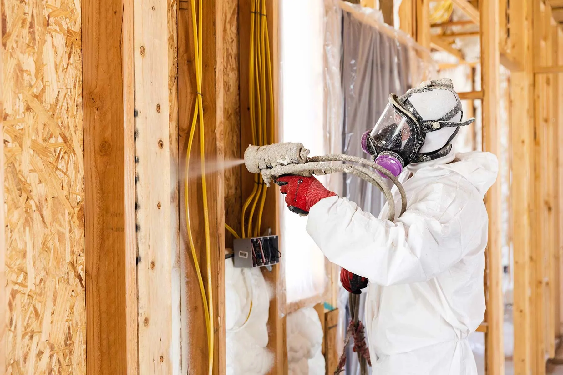 Technician spraying foam into a stud wall cavity