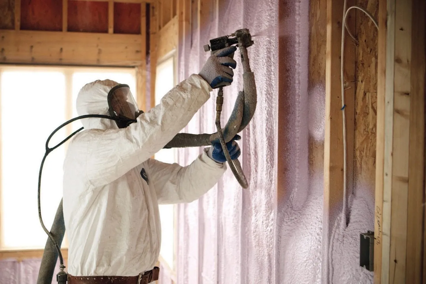 Installer spraying foam into a wall cavity beside batt insulation